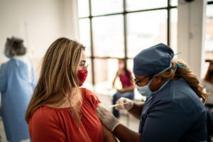 A Teenager girl wearing a nose mask being vaccinated by a medical officer who is also wearing a nose mask.