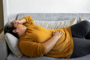 A woman is experiencing abdominal pain while sleeping on her couch due to a stomach virus.