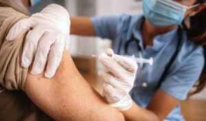 Close-up image of a blurred face of a nurse wearing a protective mask while injecting an elderly patient with a flu shot at an urgent care center.